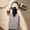 Porte-clé LIENFINITY – Agate blanche – Corde bleue Porte-clé LIENFINITY avec agate blanche, corde bleue et plaque gravée sur fond beige texturé