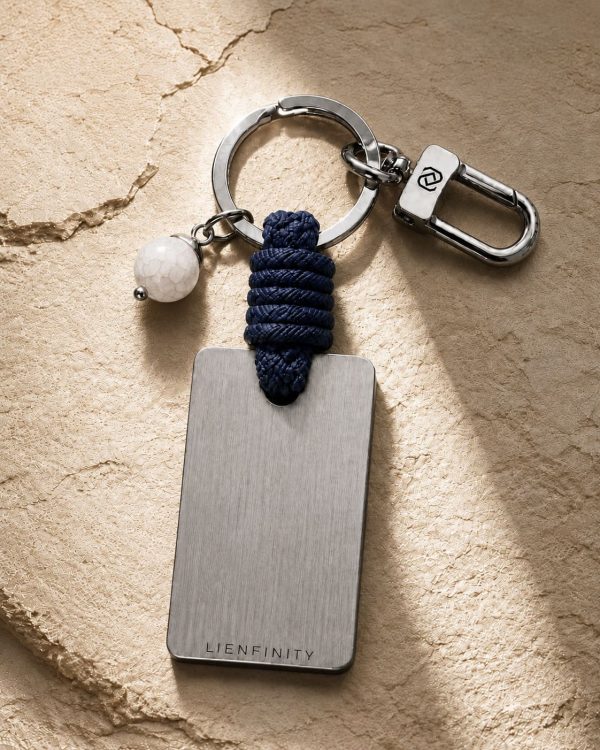 Porte-clé LIENFINITY – Agate blanche – Corde bleue Porte-clé LIENFINITY avec agate blanche, corde bleue et plaque gravée sur fond beige texturé