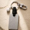 Porte-clé LIENFINITY – Agate blanche – Corde noire Porte-clé LIENFINITY avec agate blanche, corde noire et plaque gravée sur fond beige texturé