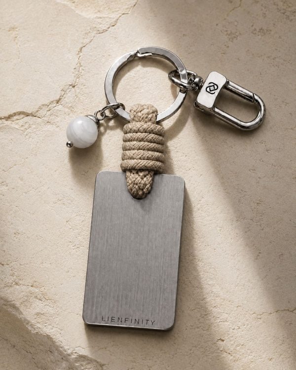 Porte-clé LIENFINITY – Agate blanche – Corde sable Porte-clé LIENFINITY avec agate blanche, corde sable et plaque gravée sur fond beige texturé