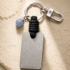 Porte-clé LIENFINITY avec calcédoine bleue, corde noire et plaque gravée sur fond beige texturé