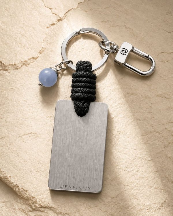 Porte-clé LIENFINITY avec calcédoine bleue, corde noire et plaque gravée sur fond beige texturé