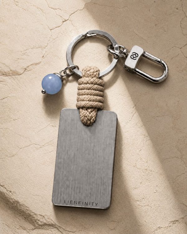 Porte-clé LIENFINITY avec calcédoine bleue, corde sable et plaque gravée sur fond beige texturé
