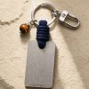 Porte-clé LIENFINITY avec œil de tigre, corde bleue et plaque gravée sur fond beige texturé