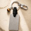 Porte-clé LIENFINITY avec œil de tigre, corde noire et plaque gravée sur fond beige texturé