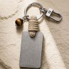 Porte-clé LIENFINITY avec œil de tigre, corde sable et plaque gravée sur fond beige texturé