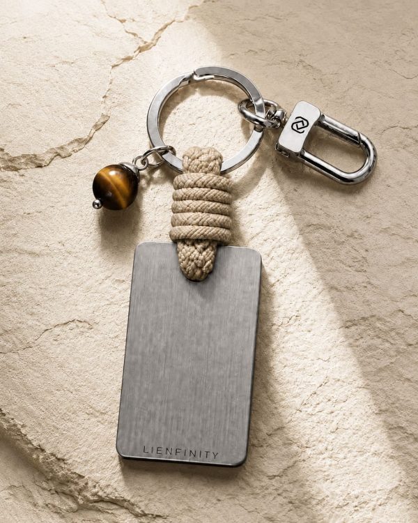Porte-clé LIENFINITY avec œil de tigre, corde sable et plaque gravée sur fond beige texturé