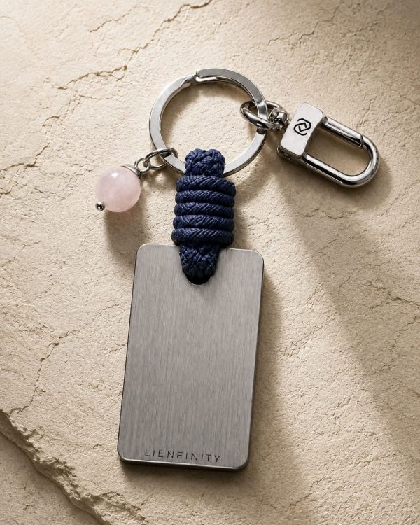 Porte-clé LIENFINITY avec quartz rose, corde bleue et plaque gravée sur fond beige texturé