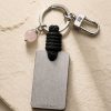 Porte-clé LIENFINITY avec quartz rose, corde noire et plaque gravée sur fond beige texturé