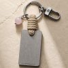 Porte-clé LIENFINITY avec quartz rose, corde sable et plaque gravée sur fond beige texturé