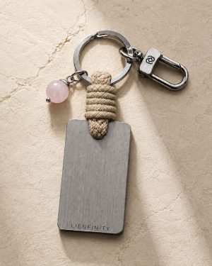 Porte-clé LIENFINITY avec quartz rose, corde sable et plaque gravée sur fond beige texturé