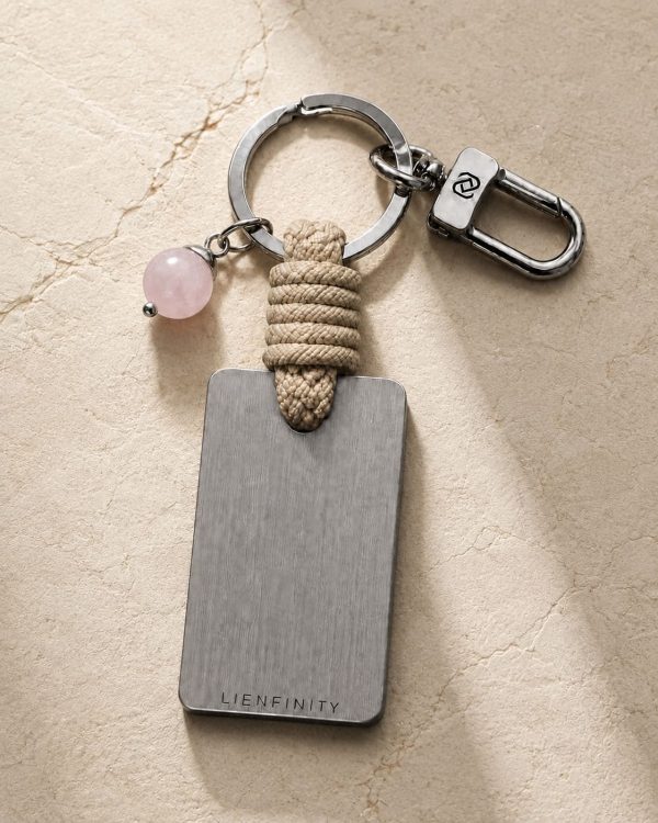 Porte-clé LIENFINITY avec quartz rose, corde sable et plaque gravée sur fond beige texturé