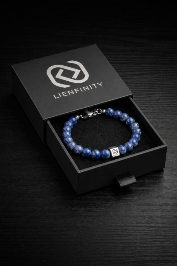 Bracelet LIENFINITY. en pierre naturelle de Lapis-Lazuli bleu intense parsemé d'éclats dorés, avec son insert de connexion en acier inoxydable 316L. Le bijou est présenté dans son écrin de luxe noir à tiroir avec le logo de la marque.