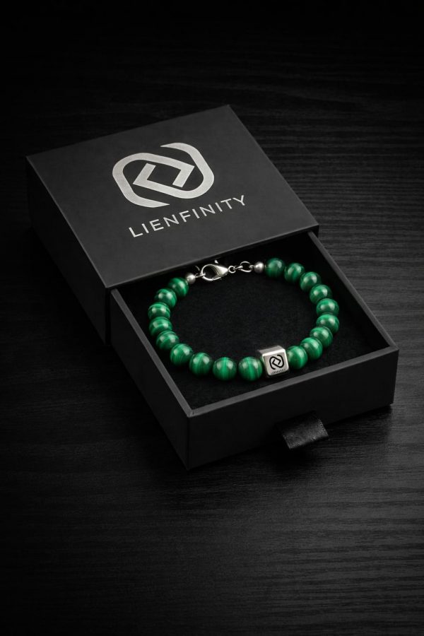 Bracelet LIENFINITY. en pierre naturelle de Malachite verte avec son insert en acier inoxydable, présenté devant son écrin de luxe noir et blanc. Le bijou met en avant les motifs circulaires naturels de la pierre et la Signature QR code gravée.