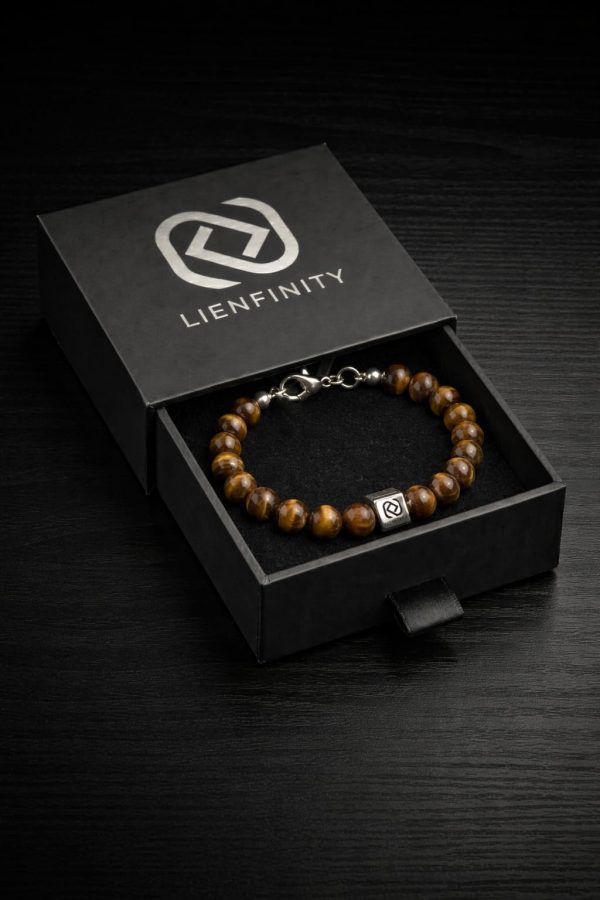bracelet-oeil-de-tigre-boite-cadeau-lienfinity Bracelet LIENFINITY en perles Œil de Tigre marron et d'une perle en acier inoxydable gravée du logo, présenté dans sa boîte cadeau noire ouverte avec lettrage argenté.