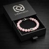 Bracelet LIENFINITY. en pierre naturelle de Quartz Rose translucide avec son insert de connexion en acier inoxydable 316L. Le bijou est présenté dans son écrin de luxe noir à tiroir avec le logo de la marque argenté.
