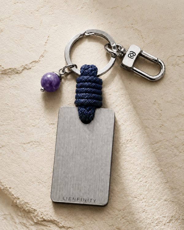 Porte-clé LIENFINITY avec améthyste violette, corde bleue et plaque gravée sur fond beige texturé