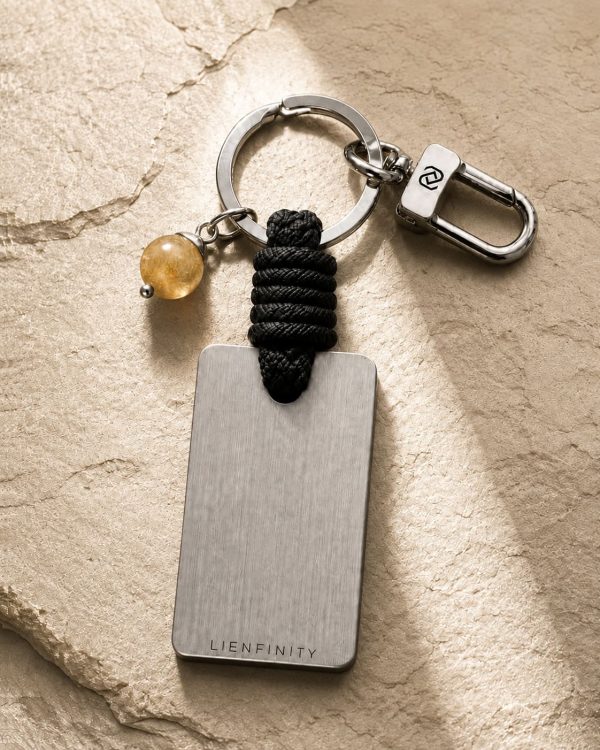 Porte-clé LIENFINITY avec citrine, corde noire et plaque gravée sur fond beige texturé