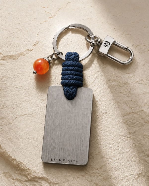 Porte-clé LIENFINITY avec cornaline orange, corde bleue et plaque gravée sur fond beige texturé