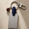Porte-clé LIENFINITY – Œil de taureau – Corde bleue Porte-clé LIENFINITY avec œil de taureau, corde bleue et plaque gravée sur fond beige texturé