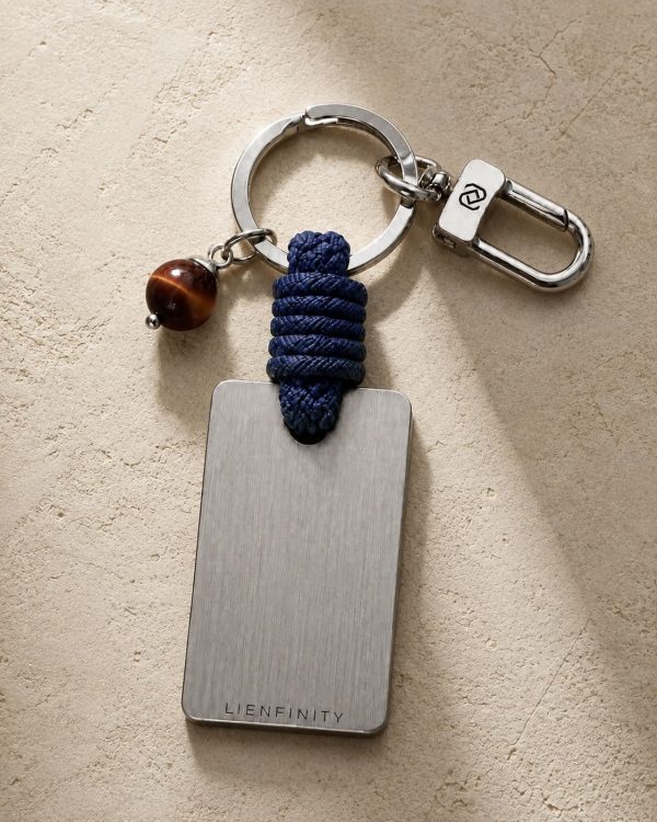 Porte-clé LIENFINITY – Œil de taureau – Corde bleue Porte-clé LIENFINITY avec œil de taureau, corde bleue et plaque gravée sur fond beige texturé