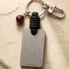 Porte-clé LIENFINITY – Œil de taureau – Corde noire Porte-clé LIENFINITY avec œil de taureau, corde noire et plaque gravée sur fond beige texturé