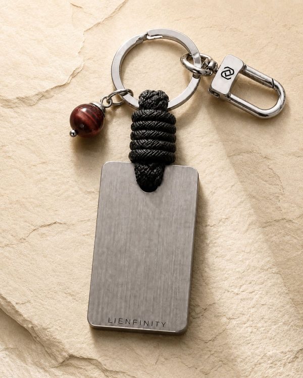 Porte-clé LIENFINITY – Œil de taureau – Corde noire Porte-clé LIENFINITY avec œil de taureau, corde noire et plaque gravée sur fond beige texturé