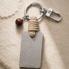 Porte-clé LIENFINITY – Œil de taureau – Corde sable Porte-clé LIENFINITY avec œil de taureau, corde sable et plaque gravée sur fond beige texturé