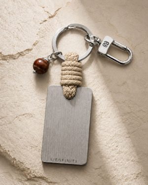Porte-clé LIENFINITY avec œil de taureau, corde sable et plaque gravée sur fond beige texturé