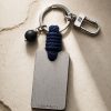 Porte-clé LIENFINITY – Onyx noir mat – Corde bleue Porte-clé LIENFINITY avec onyx noir mat, corde bleue et plaque gravée sur fond beige texturé