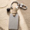 Porte-clé LIENFINITY – Onyx noir mat – Corde sable Porte-clé LIENFINITY avec onyx noir mat, corde sable et plaque gravée sur fond beige texturé