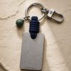Porte-clé LIENFINITY – Jade néphrite verte – Corde bleue Porte-clé LIENFINITY avec jade néphrite vert, corde bleue et plaque gravée sur fond beige texturé