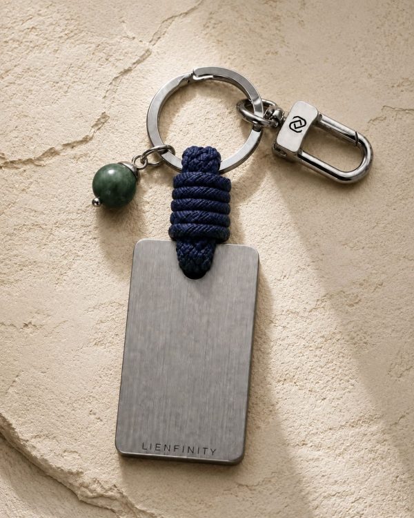 Porte-clé LIENFINITY – Jade néphrite verte – Corde bleue Porte-clé LIENFINITY avec jade néphrite vert, corde bleue et plaque gravée sur fond beige texturé