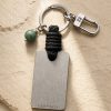 Porte-clé LIENFINITY – Jade néphrite verte – Corde noire Porte-clé LIENFINITY avec jade néphrite vert, corde noire et plaque gravée sur fond beige texturé