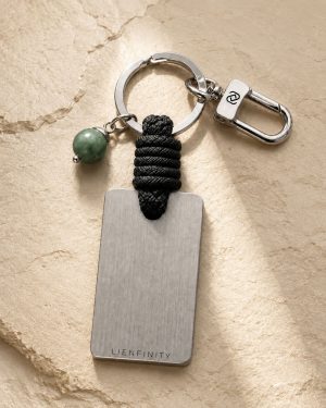 Porte-clé LIENFINITY avec jade néphrite vert, corde noire et plaque gravée sur fond beige texturé