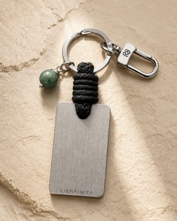 Porte-clé LIENFINITY – Jade néphrite verte – Corde noire Porte-clé LIENFINITY avec jade néphrite vert, corde noire et plaque gravée sur fond beige texturé