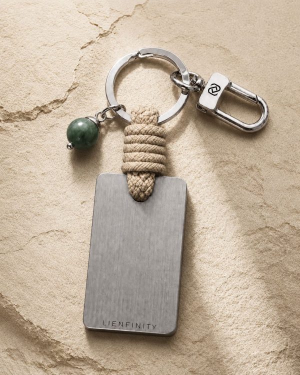 Porte-clé LIENFINITY – Jade néphrite verte – Corde sable Porte-clé LIENFINITY avec jade néphrite vert, corde sable et plaque gravée sur fond beige texturé